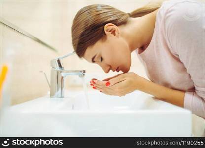 Young woman washes her face at the sink in bathroom. Female person cares for skin. Morning facial cleaning procedure. Woman washes her face at the sink in bathroom