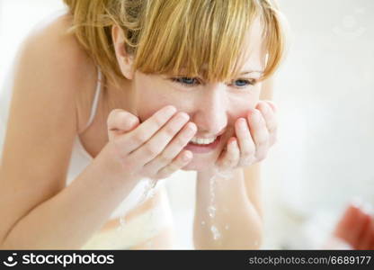 young woman washing her face in a basin and looking herself at the mirror