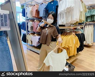 Young woman wear mask is shopping for clothes in shopping center. New normal concept