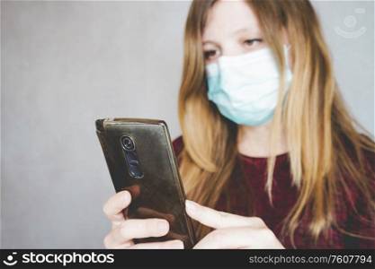 Young woman wearing a face mask and reading in her smart phone