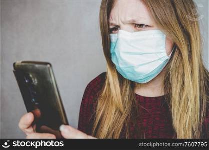 Young woman wearing a face mask and reading in her smart phone
