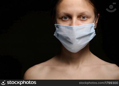 Young woman wearing a protective mask during the Coronavirus disease COVID-19 outbreak epidemic. Close up studio portrait on a black background. Young woman wearing a protective mask during the Coronavirus disease COVID-19 outbreak epidemic. Close up studio portrait on a black background.