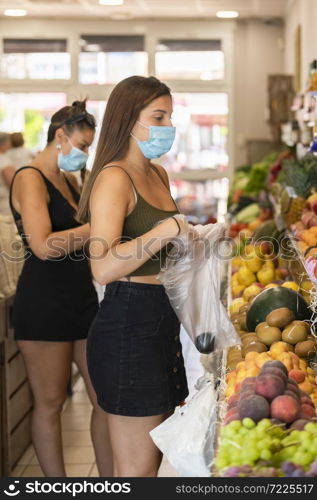 Young woman wearing a surgical mask using plastic gloves to pick up fruits at a grocery store. Safety and shopping concept.. woman wearing a surgical mask using plastic gloves to pick up fruits. Safety and shopping concept.