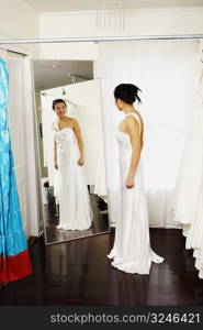 Young woman wearing a wedding dress and looking at herself in the mirror