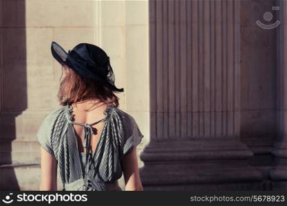 Young woman wearing an elegant dress and hat is standing in an impressive and majestic hall bathed in sunlight