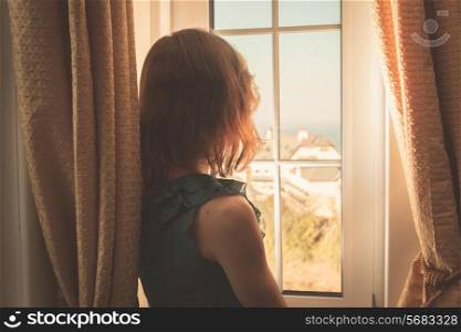 Young woman wearing an elegant dress is looking out the window