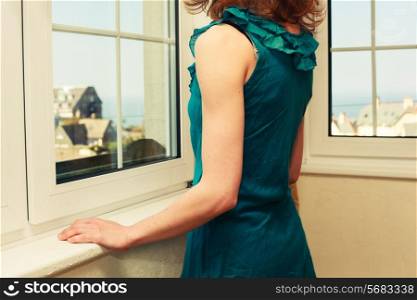 Young woman wearing an elegant dress is looking out the window