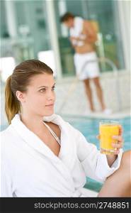 Young woman wearing bathrobe relax at swimming pool, hold juice