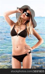 young woman wearing bikini and huge sunglasses poses like looking at the sun