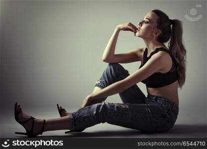 Young woman wearing black bra and blue jeans sitting on floor. S. Beautiful caucasian woman with very long hair wearing black bra and blue jeans sitting on white floor. Wavy hairstyle. Studio shot.