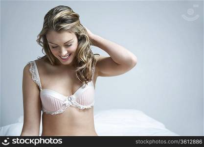 Young woman wearing bra, smiling on bed