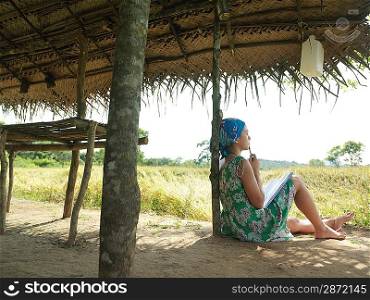 Young woman wearing dress sitting in shade of hut