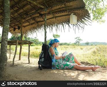 Young woman wearing dress sitting in shade of hut roof