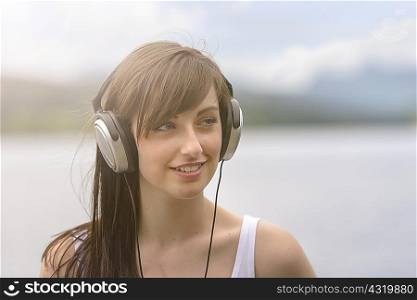 Young woman wearing headphones at lakeside under bright sunlight