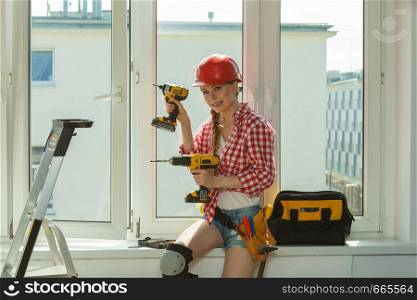 Young woman wearing helmet using power drill and tools for work at home, installing windows. Girl working at flat remodeling. Building, repair and renovation.. Woman using drill on window
