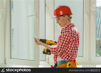 Young woman wearing helmet using power drill and tools for work at home, installing windows. Girl working at flat remodeling. Building, repair and renovation.. Woman using drill on window