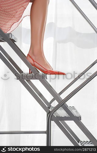 Young woman wearing high heeled shoes sitting on aluminium staircase low section side view