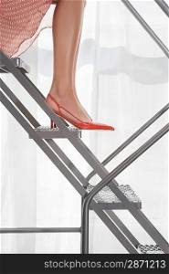 Young woman wearing high heeled shoes sitting on aluminium staircase low section side view