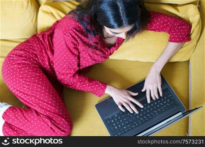 Young woman wearing pyjamas at home using laptop computer on a couch. Persian woman at home using laptop computer
