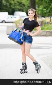 Young woman wearing roller skates holding sport bag riding in town. Female being sporty having fun during summer time.. Young woman riding roller skates holding bag