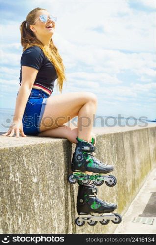 Young woman wearing roller skates relaxing after ride. Female being sporty having fun during summer time on sea coast.. Girl wearing roller skates on seaside