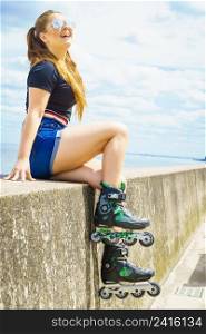 Young woman wearing roller skates relaxing after ride. Female being sporty having fun during summer time on sea coast.. Girl wearing roller skates on seaside