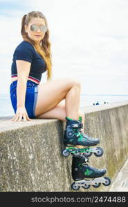 Young woman wearing roller skates relaxing after ride. Female being sporty having fun during summer time on sea coast.. Girl wearing roller skates on seaside