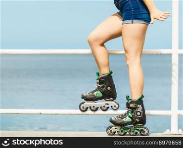 Young woman wearing roller skates relaxing after ride. Fit female having fun during summer time on sea coast.. Girl wearing roller skates on seaside