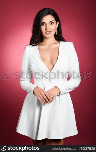 Young woman wearing short white dress on red background. Brunette girl with long hair and wavy hairstyle