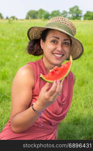 Young woman wearing straw hat eating fresh red melon in nature