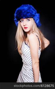 Young woman wearing summer dress and blue winter hat on black background