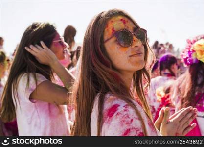 young woman wearing sunglasses mess with holi color looing camera