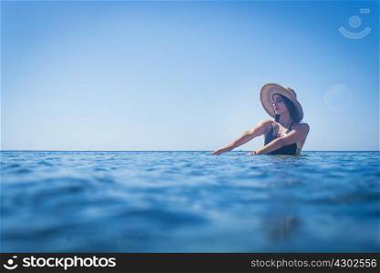 Young woman wearing sunhat wading in deep blue sea, Villasimius, Sardinia, Italy