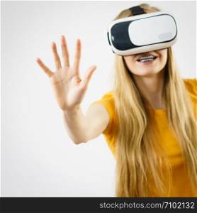 Young woman wearing virtual reality goggles headset, vr box, stretching arms. Studio shot on gray. Concept of connection, technology, new generation and progress.. Girl wearing virtual reality goggles.
