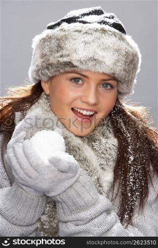 Young Woman Wearing Warm Winter Clothes And Fur Hat Holding Snowball In Studio