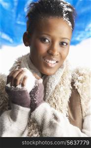 Young Woman Wearing Warm Winter Clothes Holding Snowball In Studio