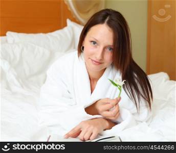 young woman wearing white bathrobe in bed reading a book