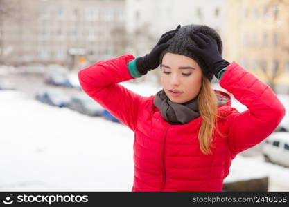 Young woman wearing winter clothes holding her head looking worried, outside shot during snowy weather.. Woman wearing winter clothes outside holding her head