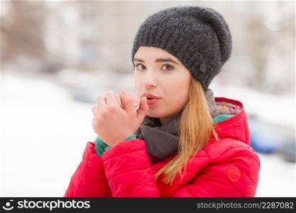 Young woman wearing winter clothes warming up her hands, outside shot during cold snowy weather.. Woman wearing winter clothes outside warming her hands
