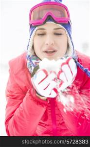 Young woman wearing winter coat blowing snow outdoors