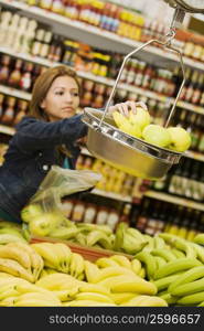 Young woman weighing apples on a weighing scale in a supermarket