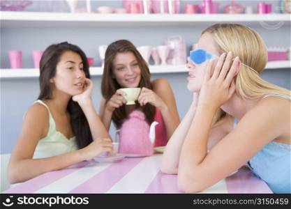 Young woman with a hangover sitting at a table with two friends