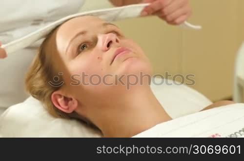Young woman with a headwrap being put on before facial spa procedures
