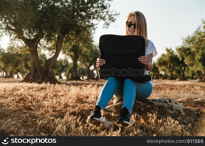 Young woman with a laptop case seated in the olive tree field