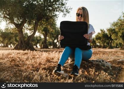 Young woman with a laptop case seated in the olive tree field