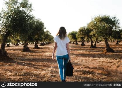 Young woman with a laptop case through the olive field
