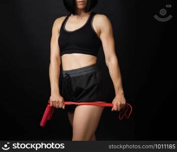 young woman with a sports figure in black uniform holds a red rope for jumping, low key