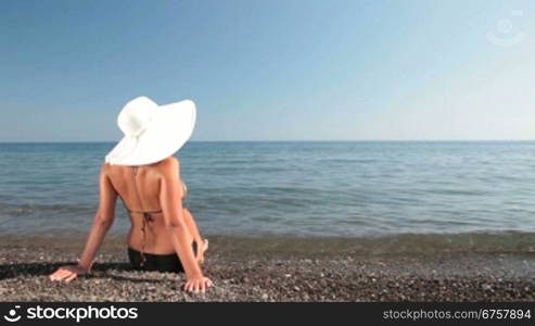 young woman with a white hat sitting on the beach