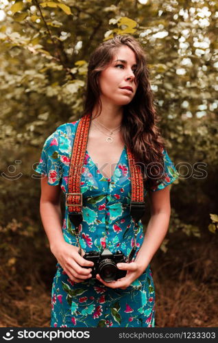 Young woman with analog camera wearing a dress in the forest