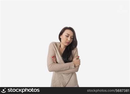 Young woman with arms crossed shivering against gray background